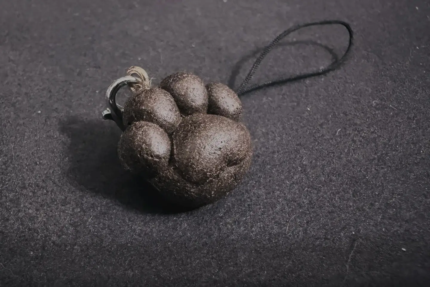 深灰色背景上的棕色肉球吊飾，連接金屬環與黑色掛繩