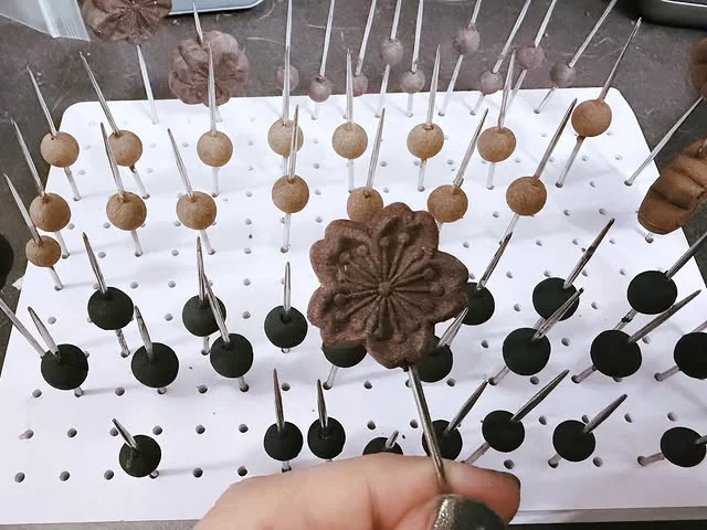 白色多孔板上插著多顆珠件,前景手持花形合香件